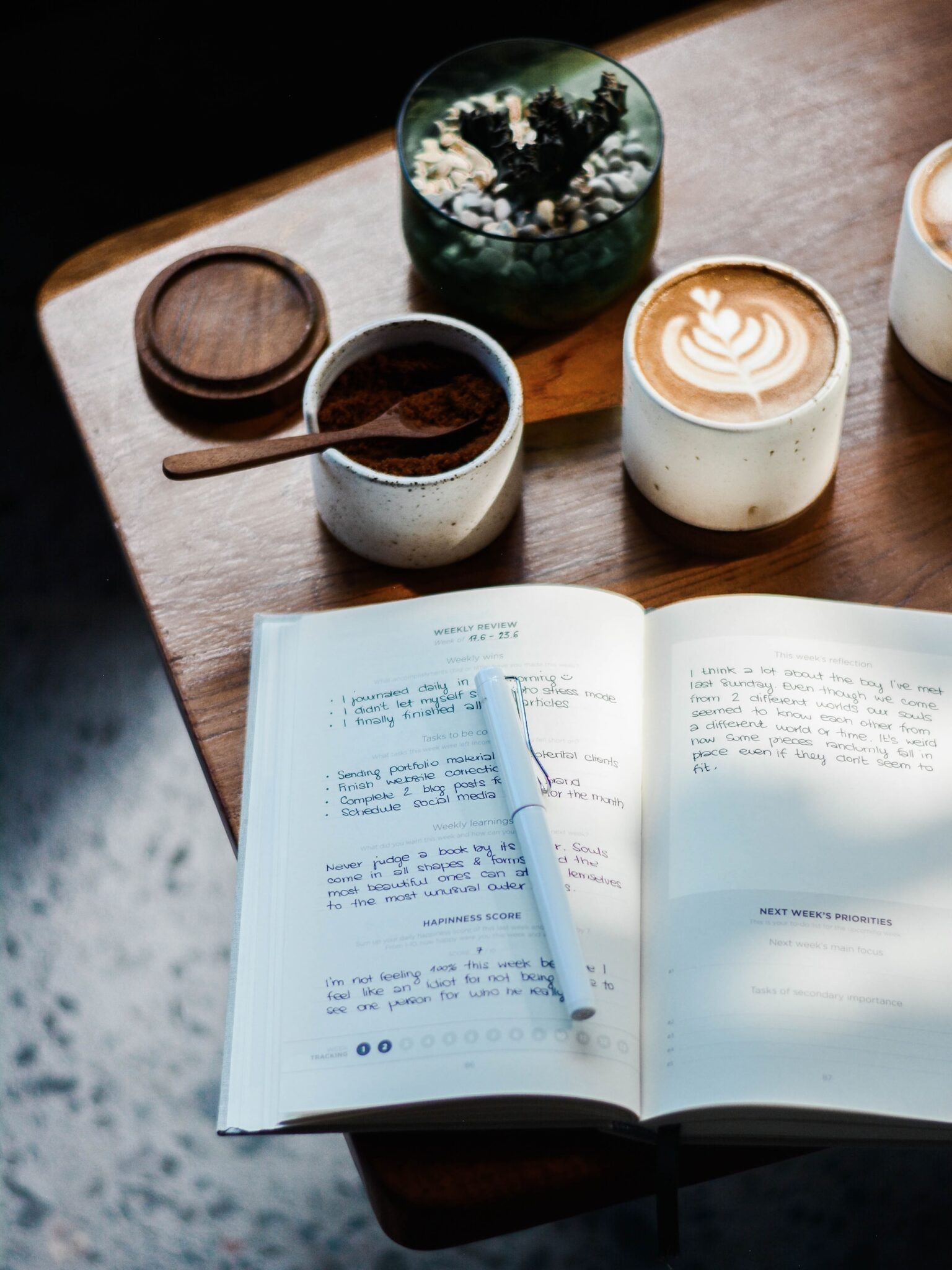 A journal with a pen and a cup of coffee on a wooden table. Self care help. Support for new parents.