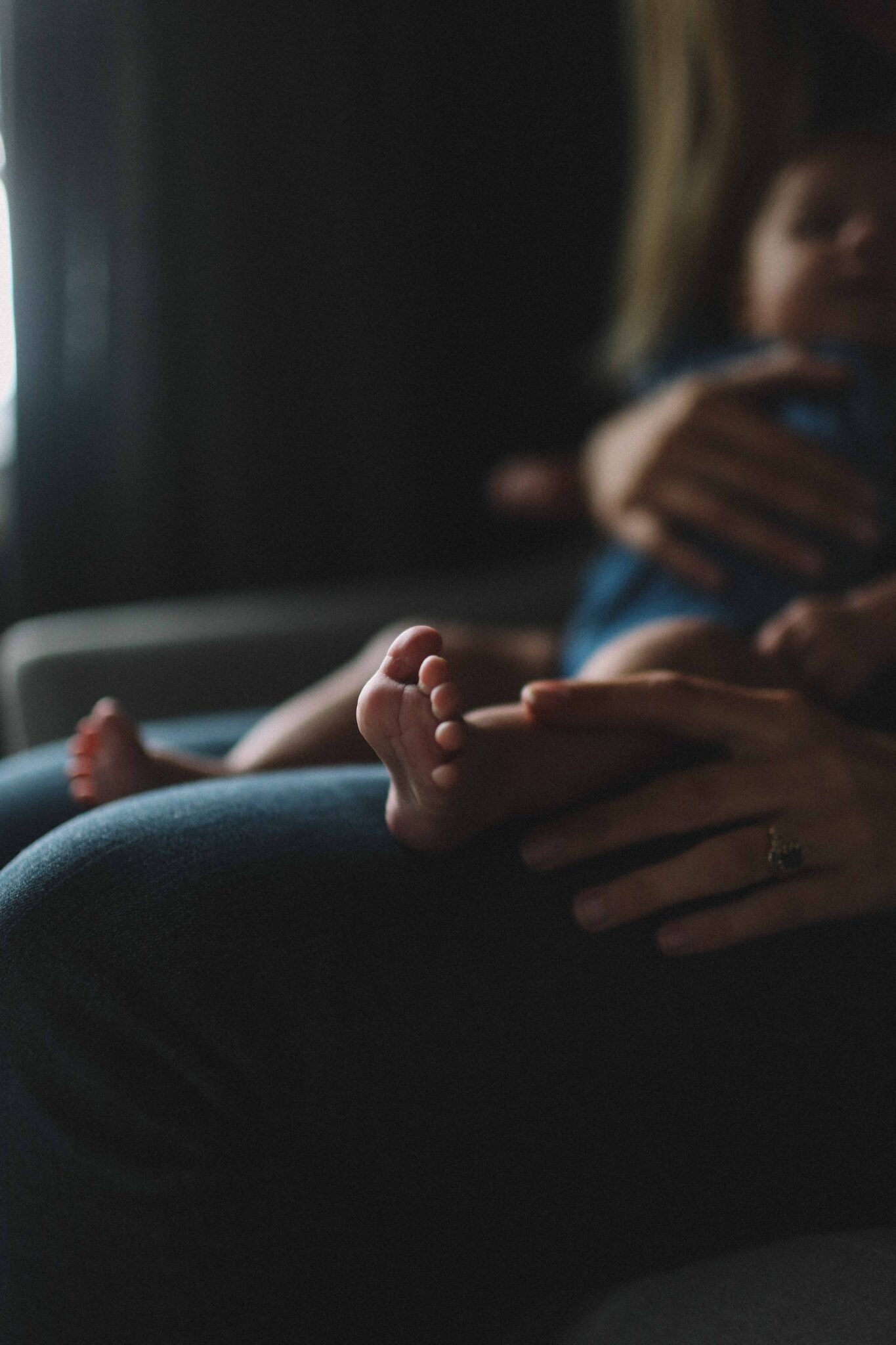 A new mom with long hair, sitting on the couch with her infant on her lap. New beginnings. Motherhood journey. Mental health care for moms.