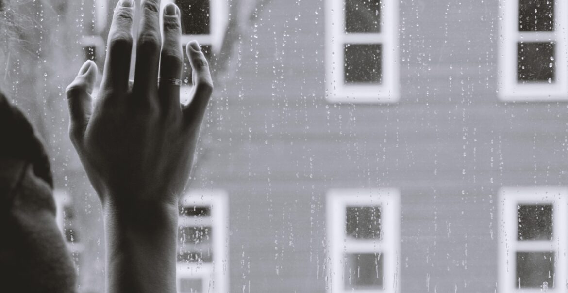 a person looking out the window while it's raining with their hand on the glass. Depression treatment. Postpartum depression counselor.