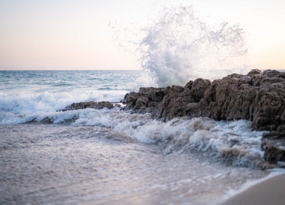 A wave hit some large rocks on the beach and ocean water sprayed everywhere. Rainbow baby therapist. Grief counselor.