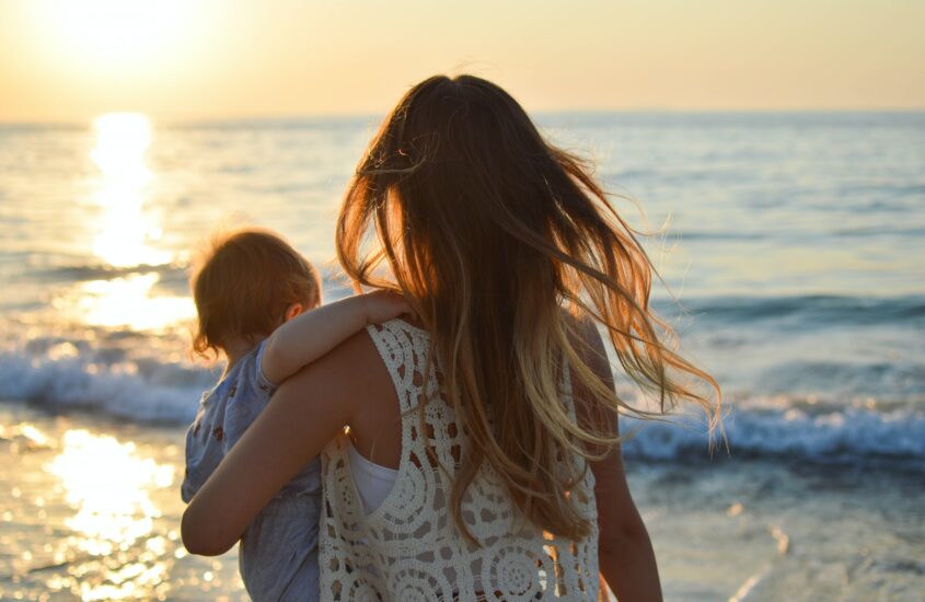 A mom holding her child while looking at the waves at the beach. Therapy for new parents. Postpartum support.