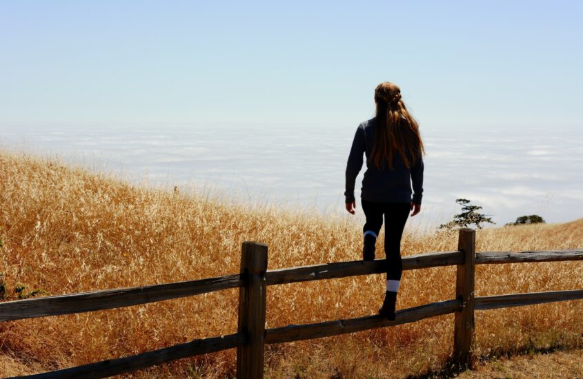 Girl on a hill stepping over a low fence. Overcome codependency and addictive behaviors. EMDR therapy for trauma.
