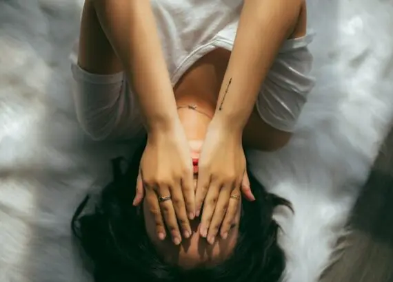 A woman lying on her stomach, hands covering her face, seeking anxiety treatment.