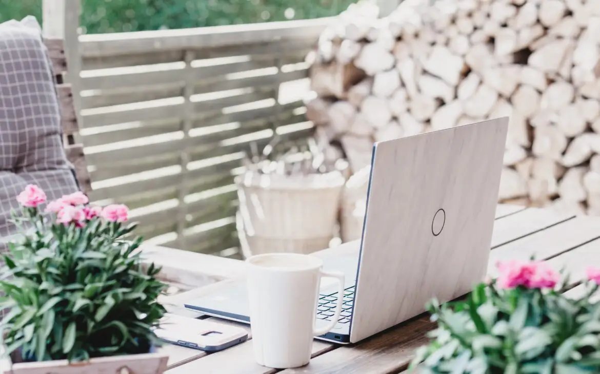 A laptop on a wooden table with flowers and a cup of coffee, creating a serene workspace for online therapy.