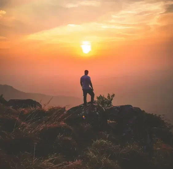 A man standing on a mountain peak, enjoying the breathtaking sunset view.