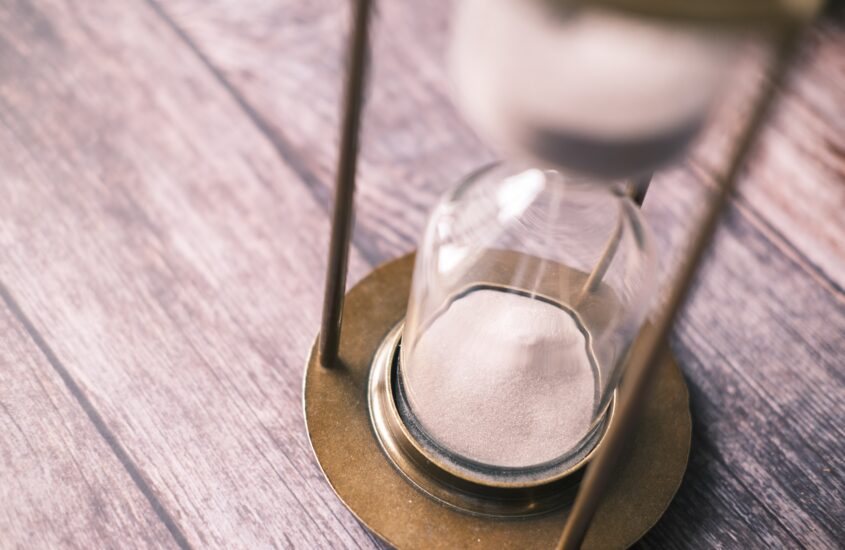 An hourglass with sand on a wooden table, symbolizing the passage of time and reflecting on a past mistakes.