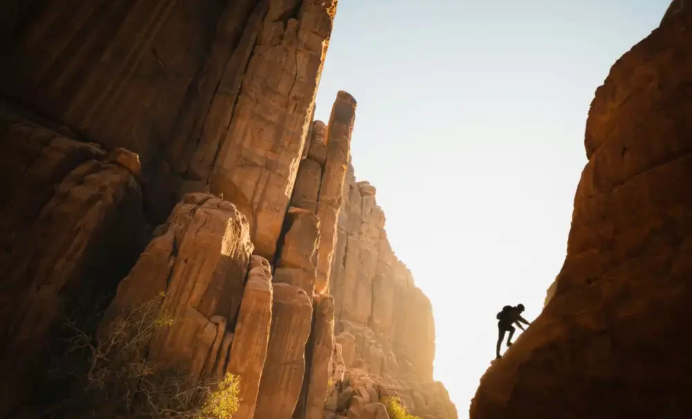 A man scaling a desert rock structure, symbolizing overcoming perfectionism by accepting imperfections.