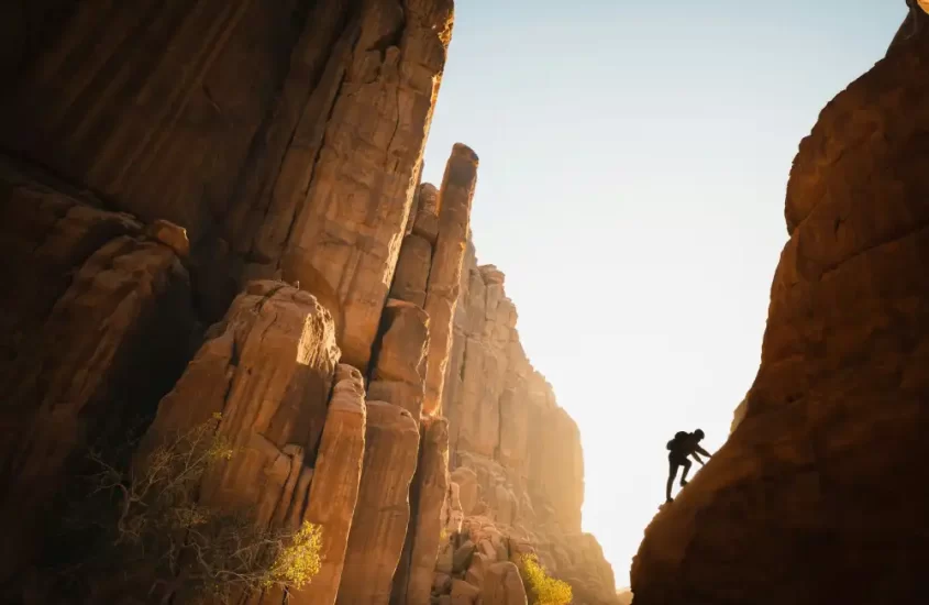 A man scaling a desert rock structure, symbolizing overcoming perfectionism by accepting imperfections.